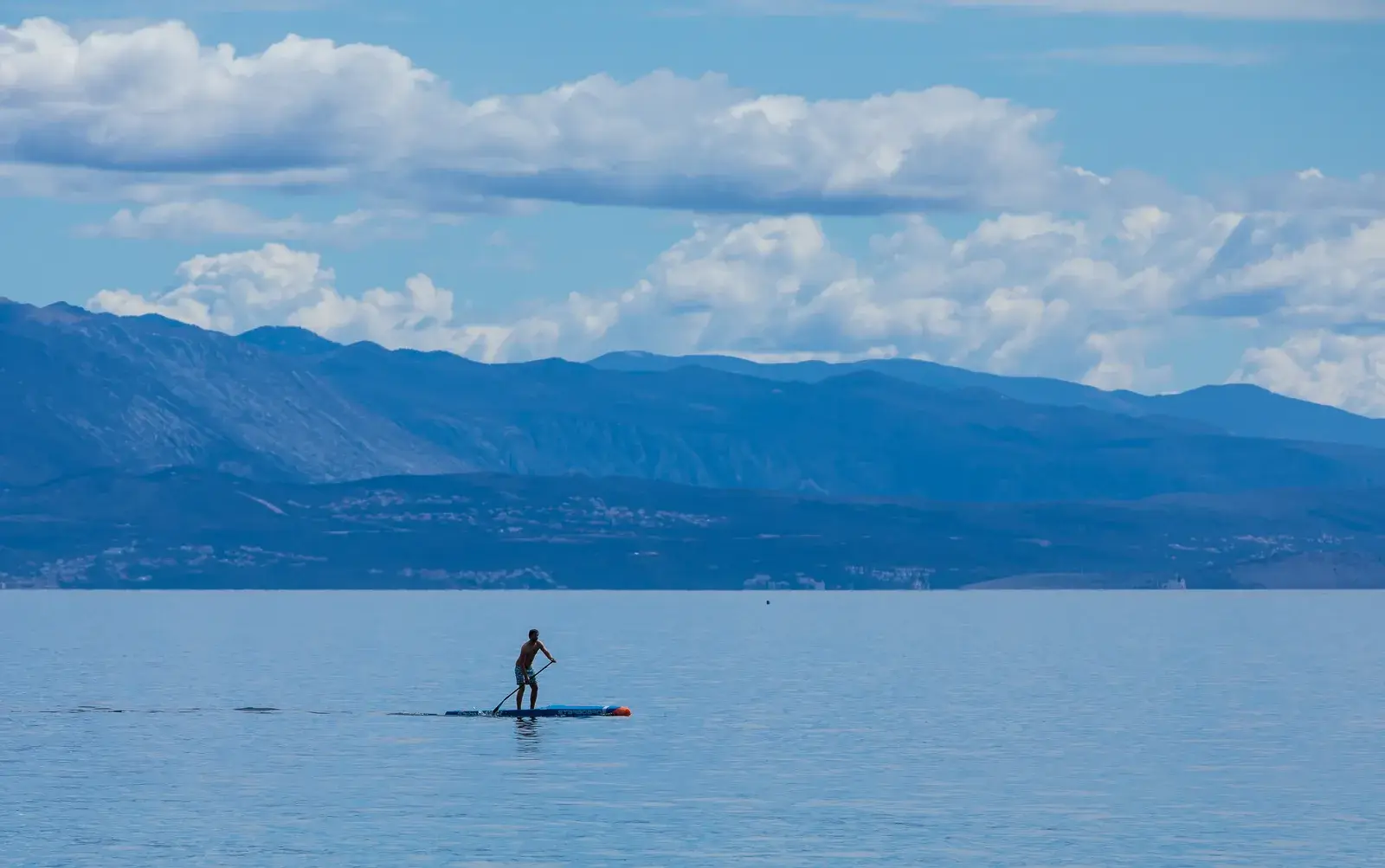 Una persona pagaia in stand up paddle su un mare piatto vicino alla costa