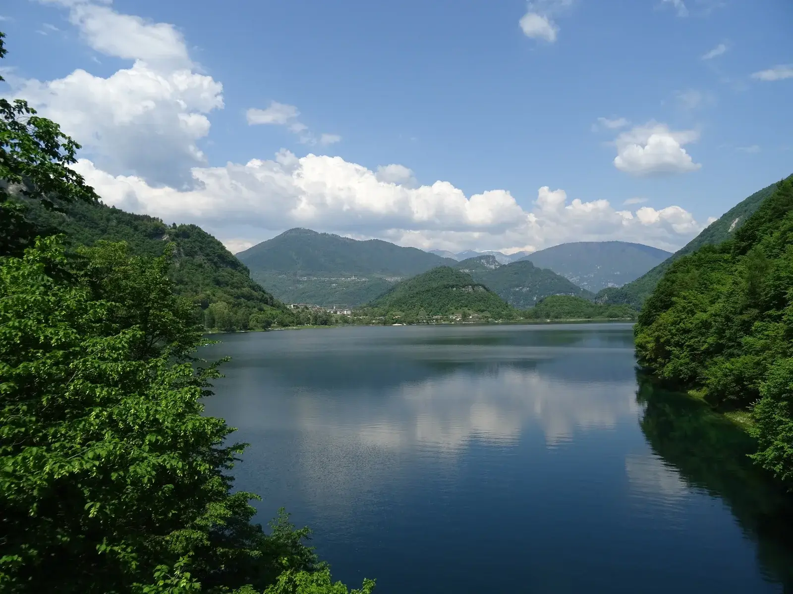 Il Lago di Corlo in una giornata estiva, con i versanti boscosi che scendono nell’acqua