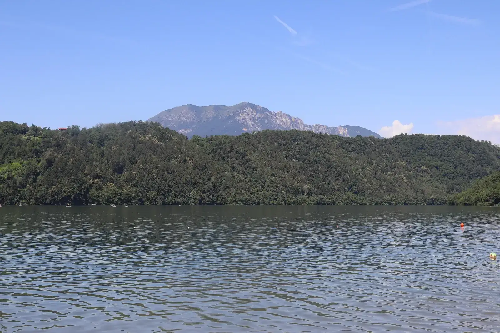 Il Lago di Levico visto dalla riva, con la sponda boscosa e le montagne della Valsugana