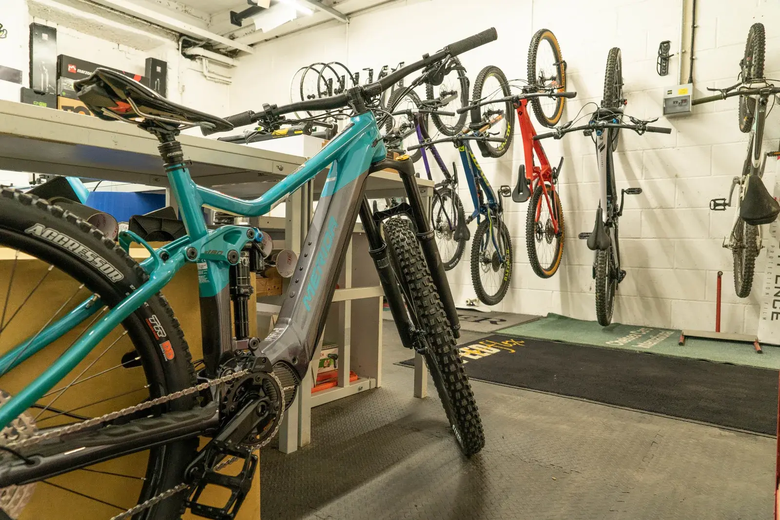 Una e-bike da montagna in primo piano e altre bici appese al muro di un’officina
