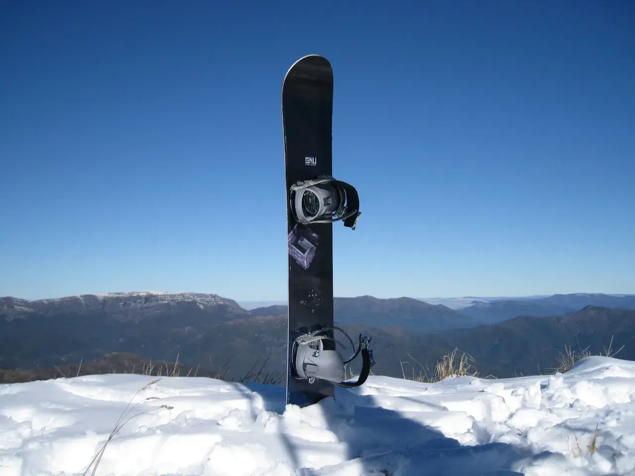 Una tavola da snowboard piantata nella neve con le montagne sullo sfondo