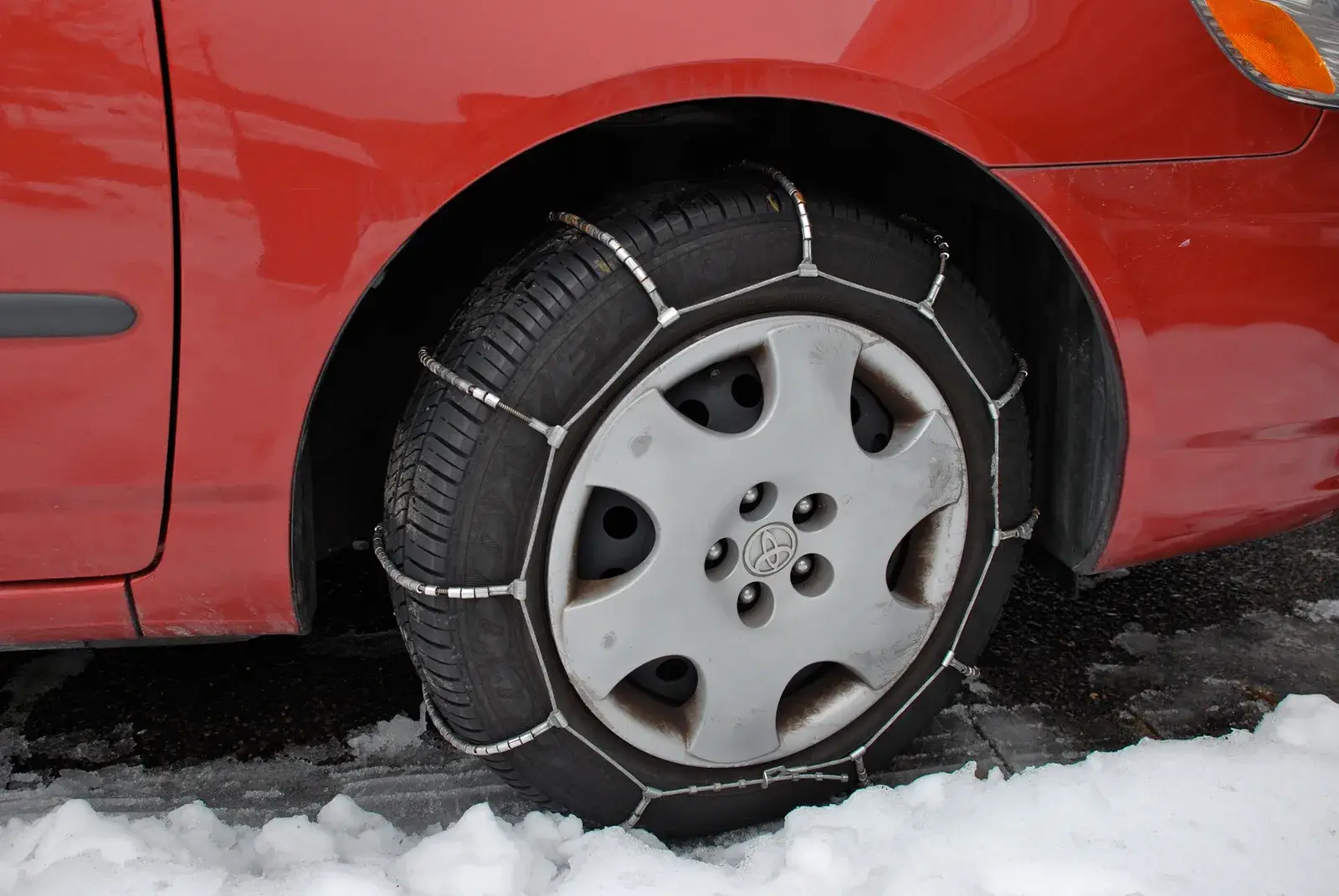 Catene da neve montate sulla ruota di un’auto rossa su strada innevata