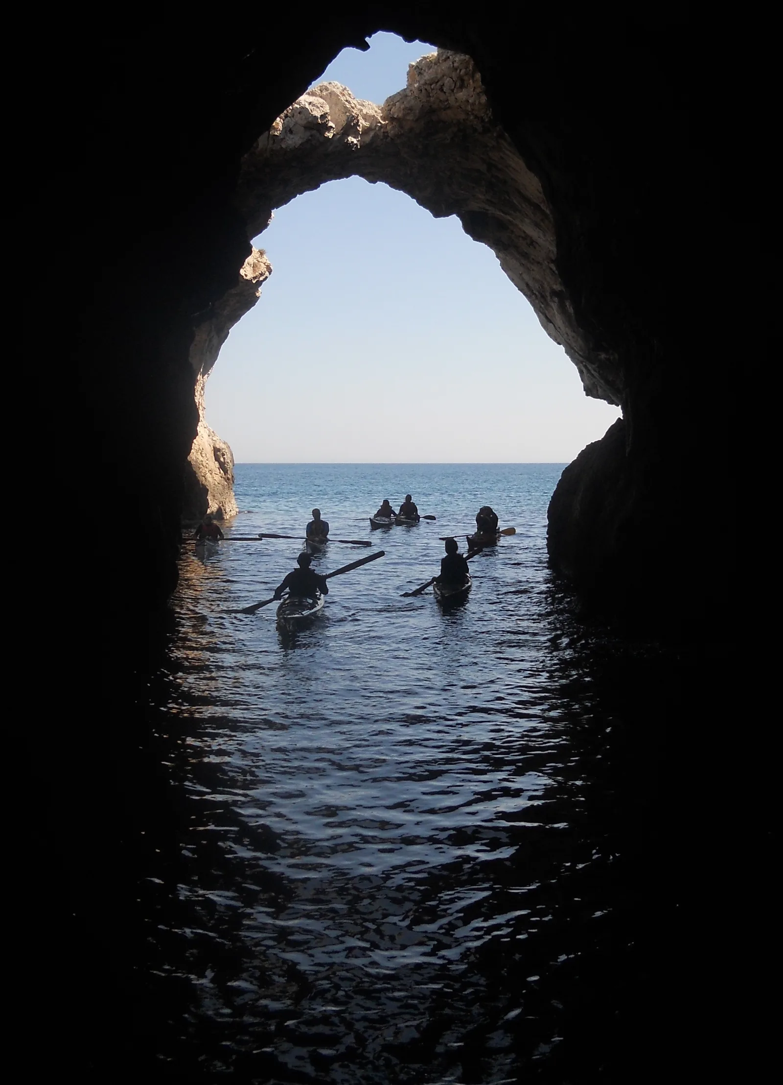 Un kayak da mare entra in una grotta marina lungo una costa rocciosa italiana