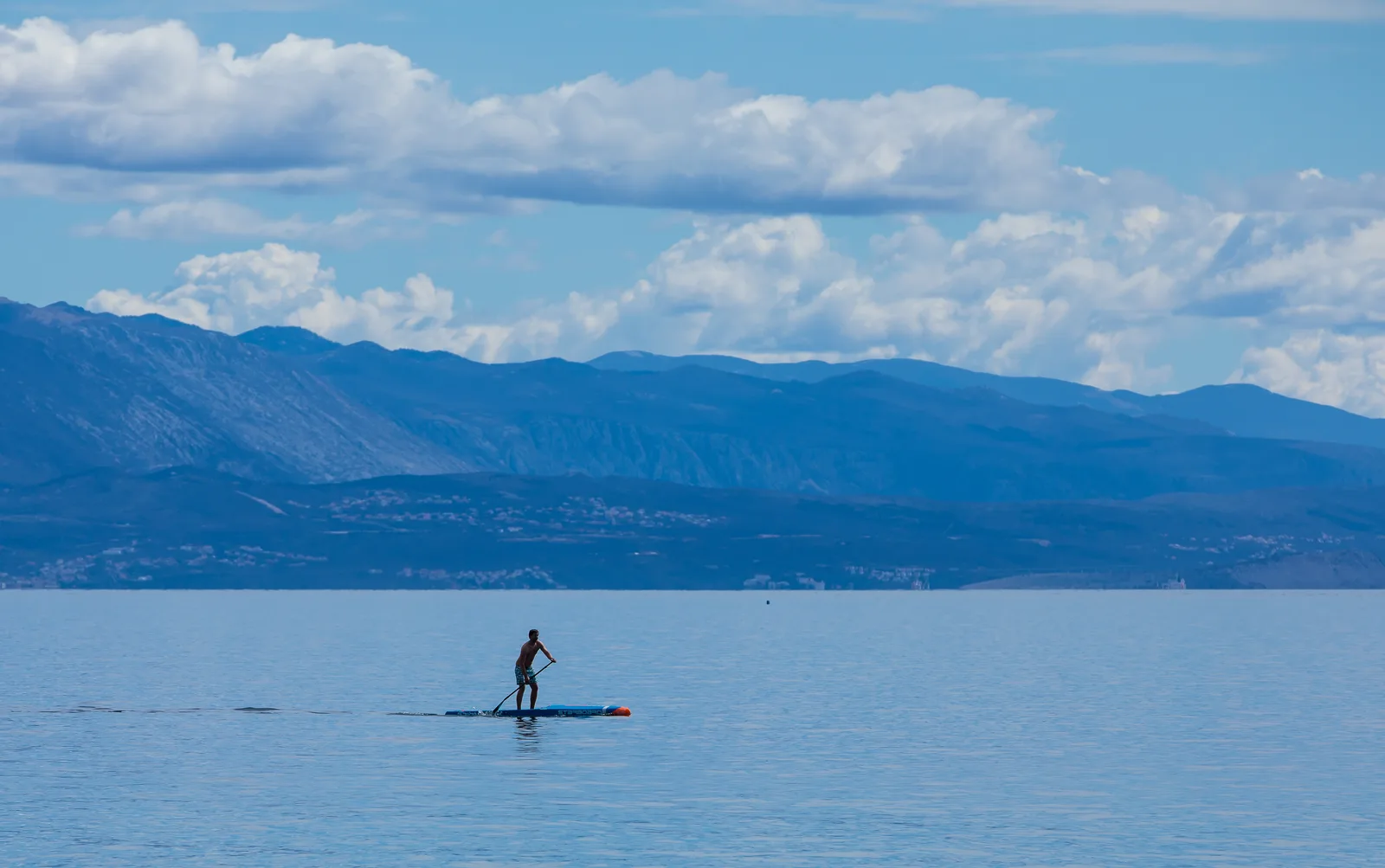 Una persona pagaia in stand up paddle su un mare piatto vicino alla costa
