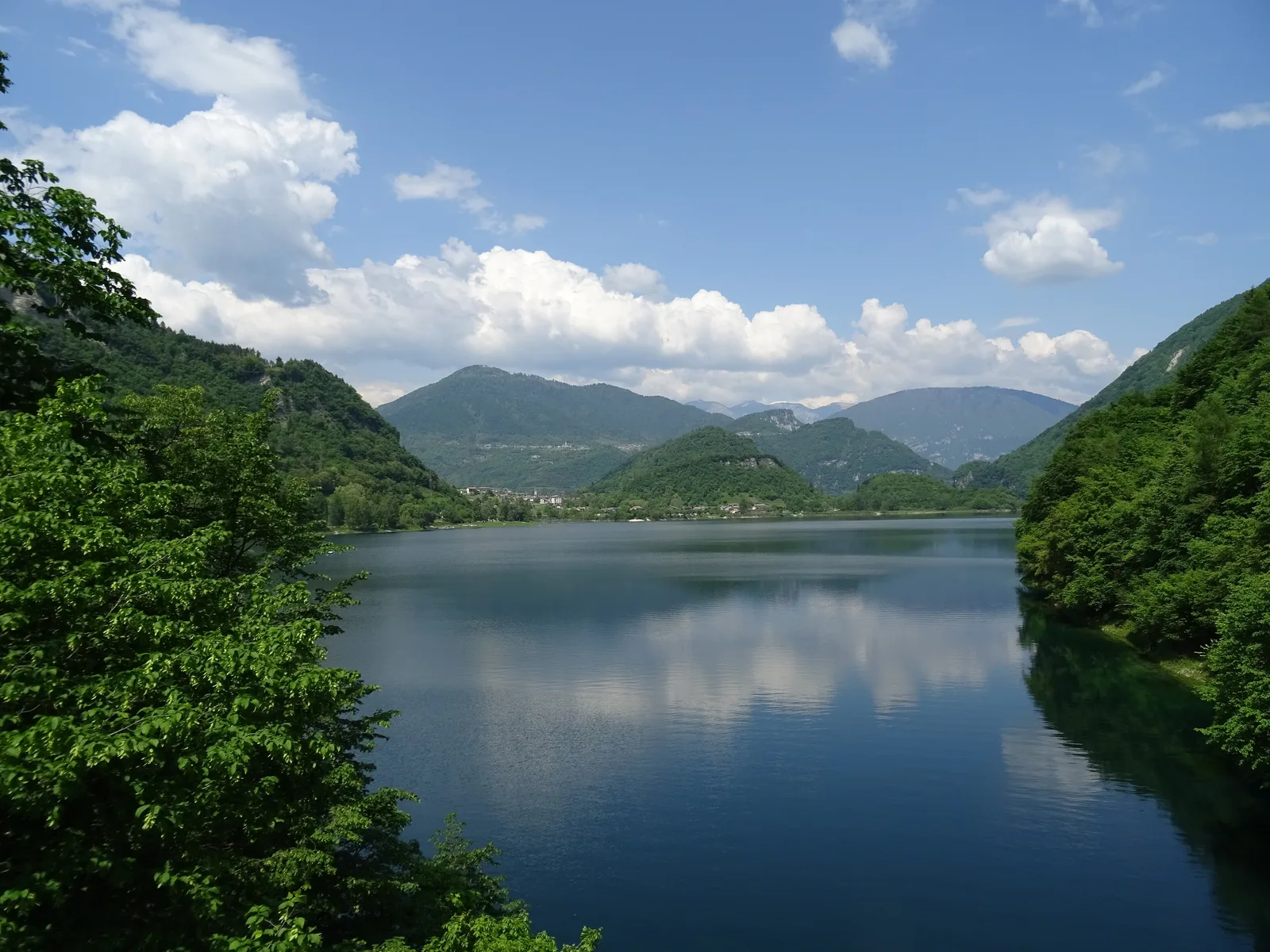 Il Lago di Corlo in una giornata estiva, con i versanti boscosi che scendono nell’acqua