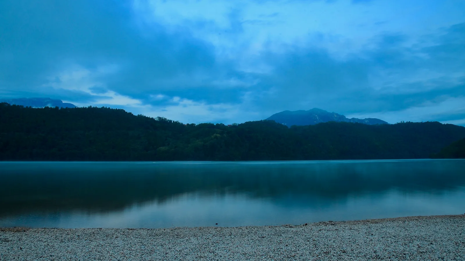 Il Lago di Levico prima dell’alba, con acqua a specchio e spiaggia di ghiaia