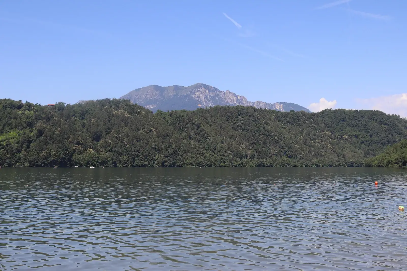 Il Lago di Levico visto dalla riva, con la sponda boscosa e le montagne della Valsugana